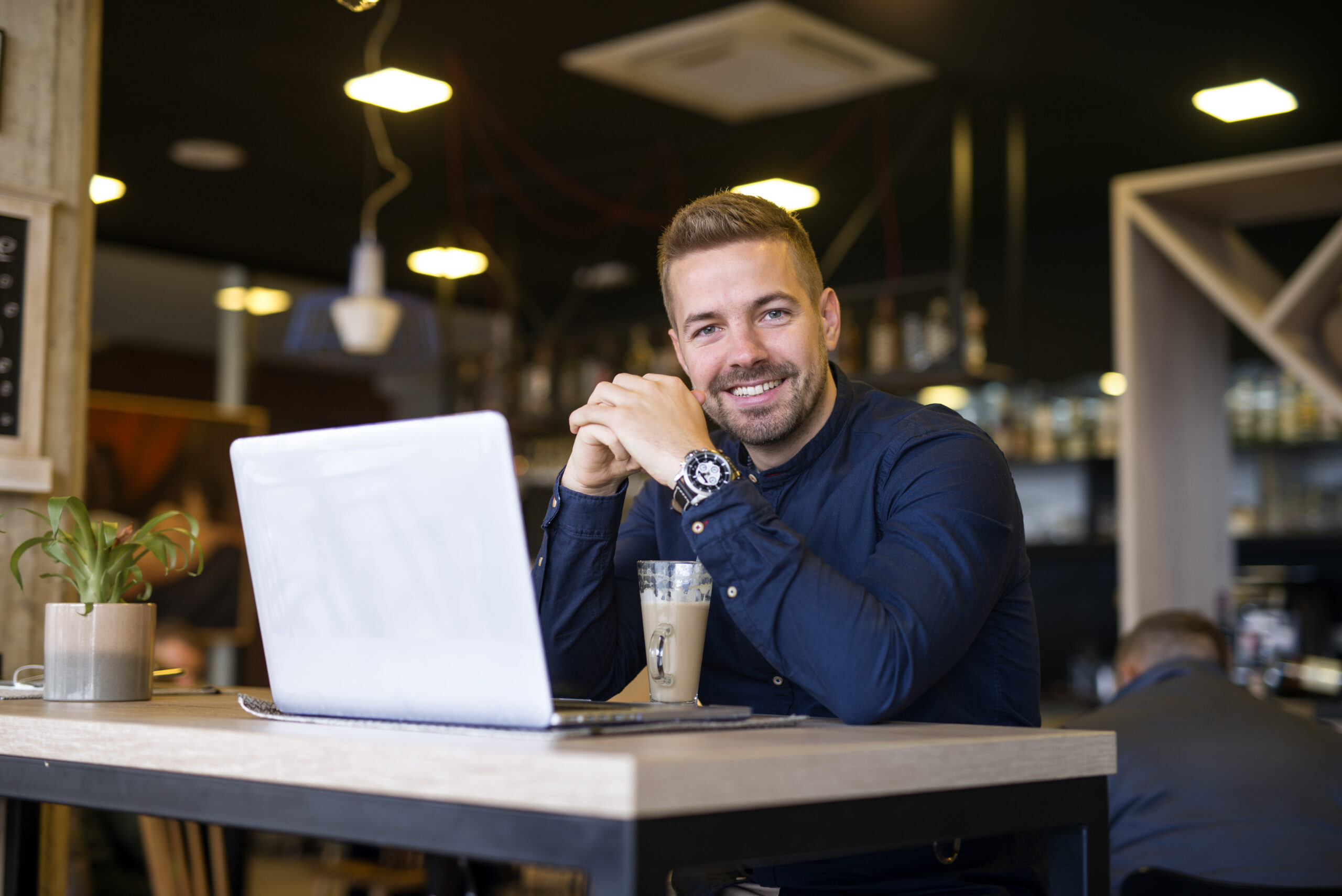 Portrait of smiling man sitting in a cafe bar with his laptop computer. São Gonçalo do Rio Abaixo lança o Programa Crescer Sem Juros, oferecendo linhas de crédito sem juros para MEIs, micro e pequenas empresas. Ação visa fortalecer a economia local e gerar empregos